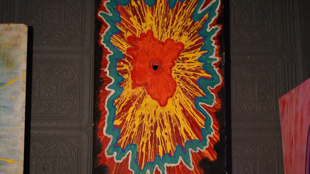Abstract red, yellow, black painting with blue border on patterned wall.