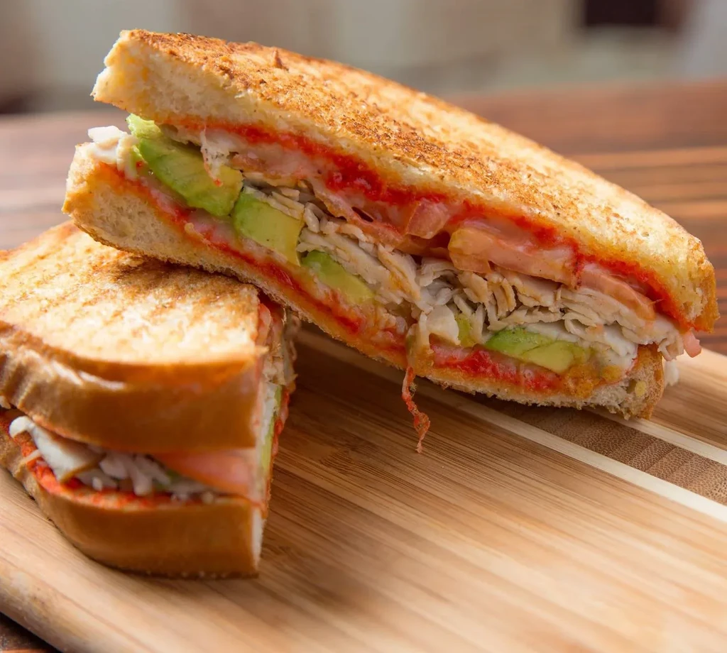 Halved grilled sandwich with avocado, shredded chicken, and red sauce.