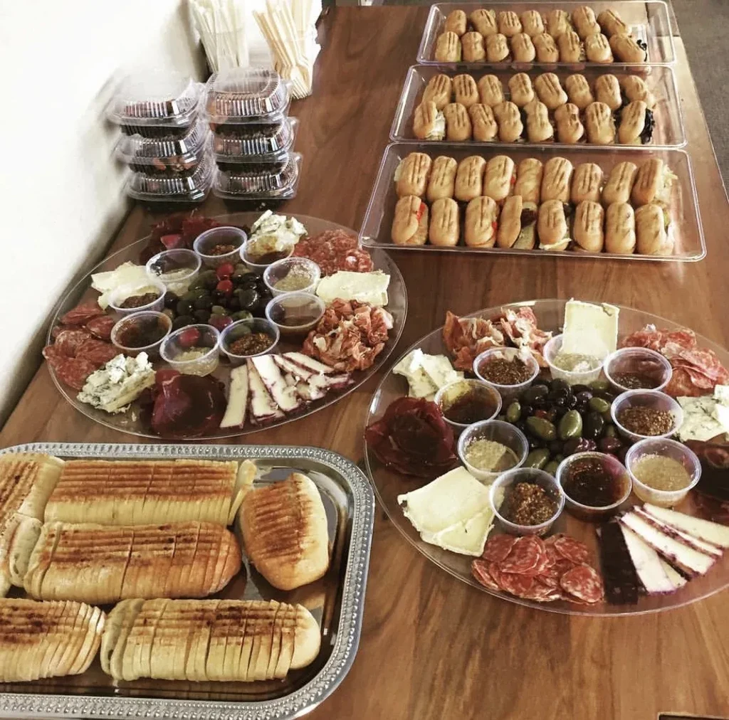 Large catering spread with grilled bread, charcuterie, and mini-sandwiches.