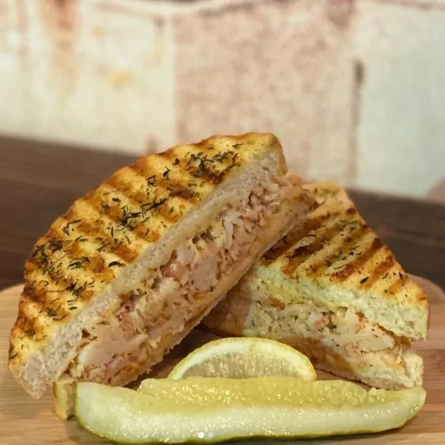 Grilled sandwich with chunky filling, lemon, pickle on a wooden board.