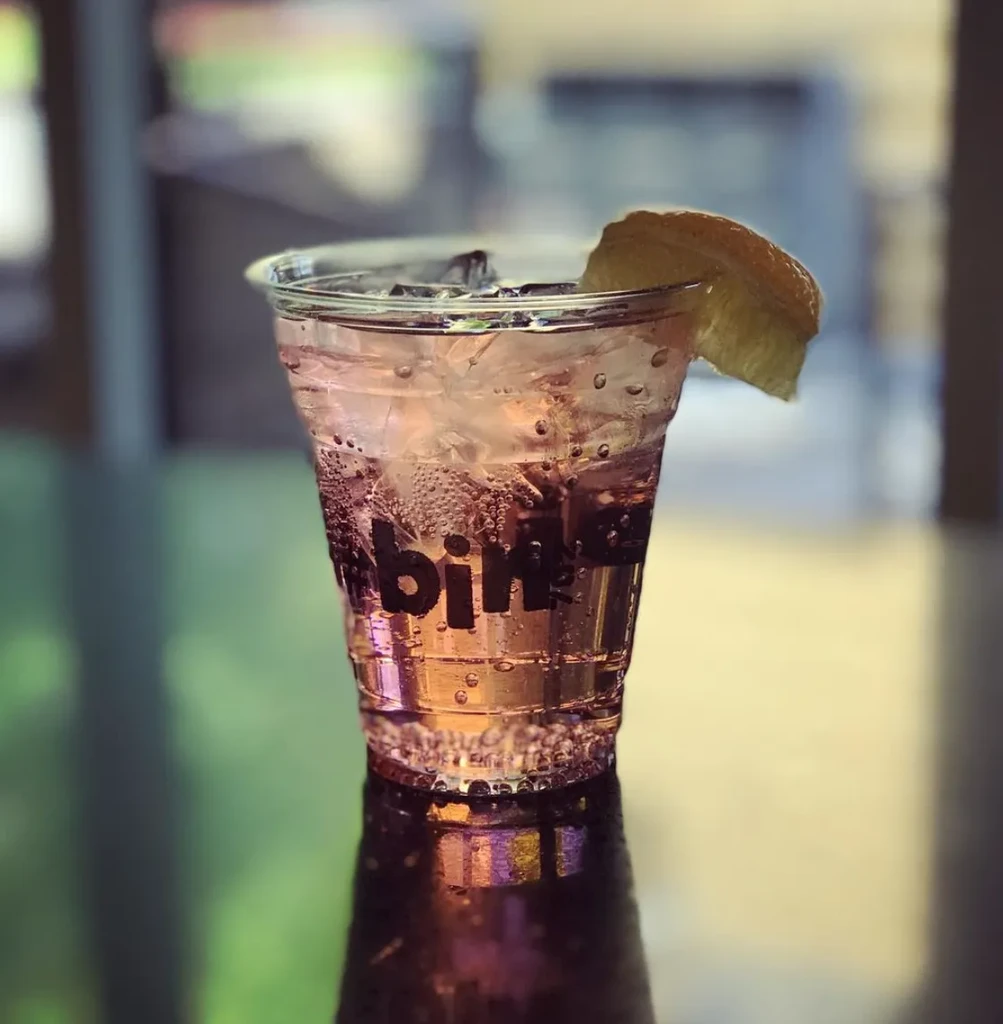 Pink drink in plastic cup with ice, lemon wedge, "bin" printed.