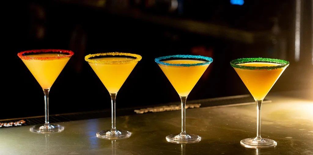 Four martini glasses with yellow-orange drinks and colorful sugar rims.