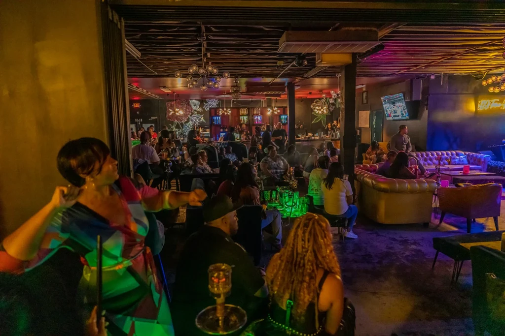 Lively, neon-lit lounge scene with patrons, bar, and hookah pipes.