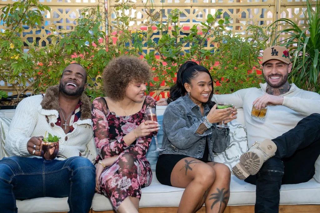 Four smiling people enjoy drinks on an outdoor patio couch.