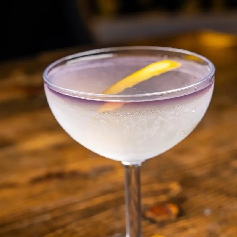 Cold, two-toned white and purple cocktail with a lemon peel.