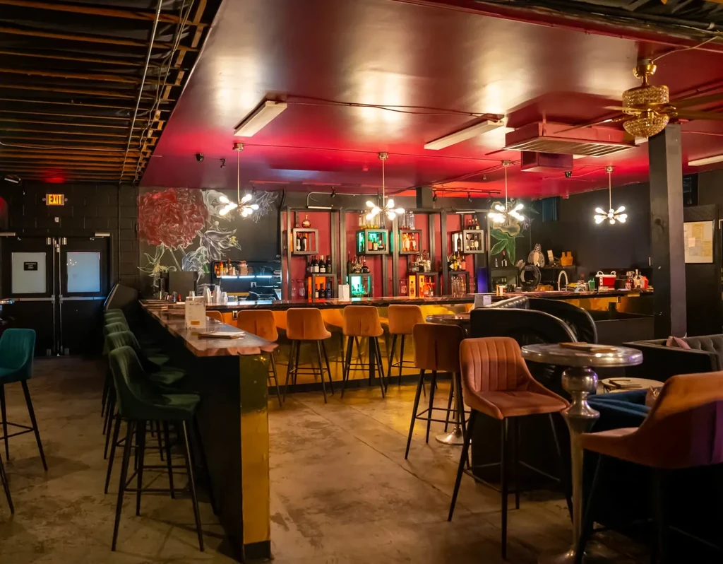 Dark, stylish bar interior with velvet stools, red ceiling, and peony mural.