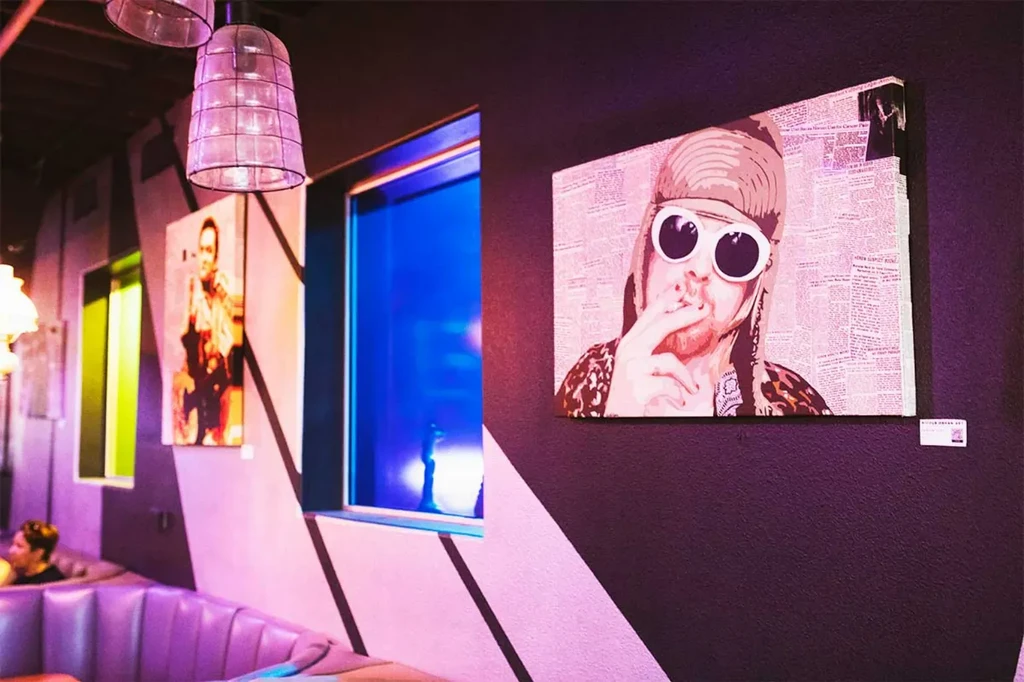Purple-lit interior with pop-art Kurt Cobain portrait and blue window glow.