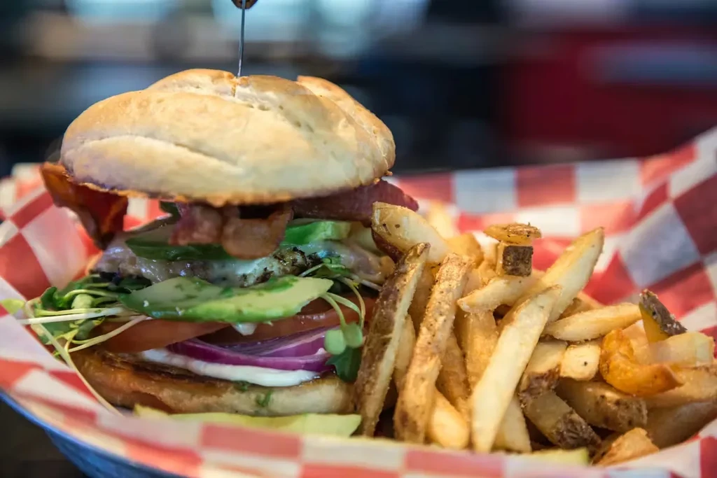 A gourmet burger with bacon, avocado, and fries in a checkered basket.