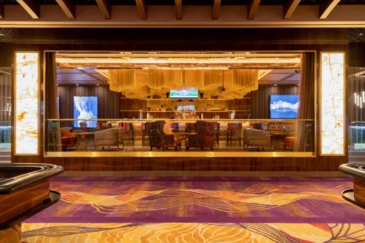 Lavish bar interior with patterned carpet, gold ceiling fixture, and screens.