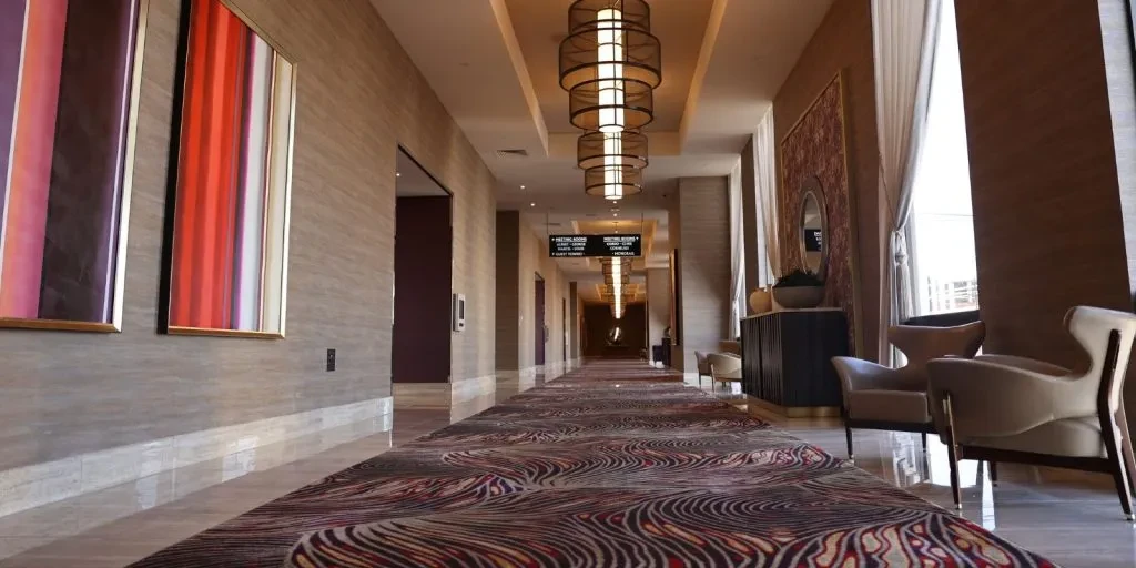 Luxurious hotel hallway with patterned carpet, chandeliers, artworks, and lounge seating.