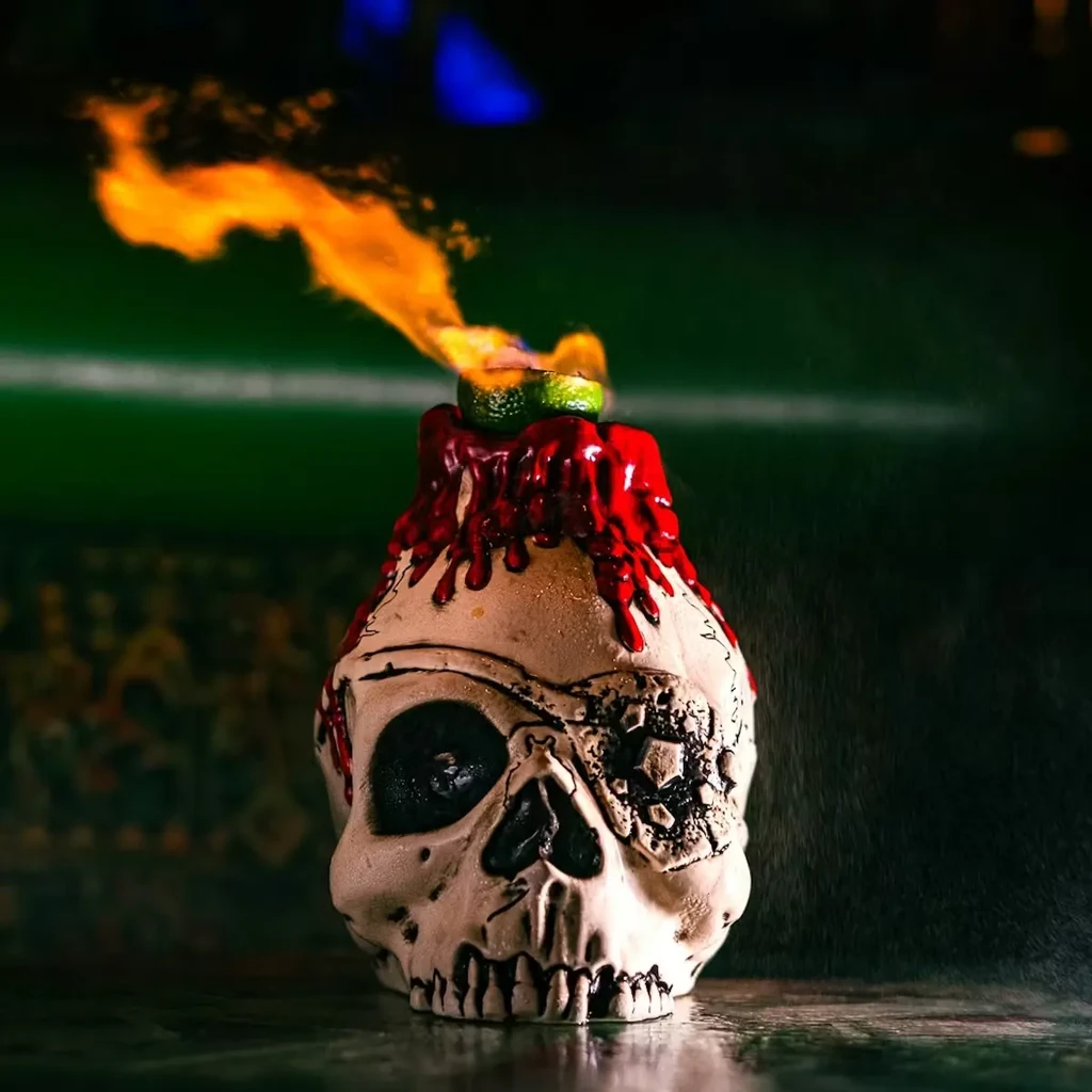 Close-up of a skull mug cocktail with red drips and a flaming lime.
