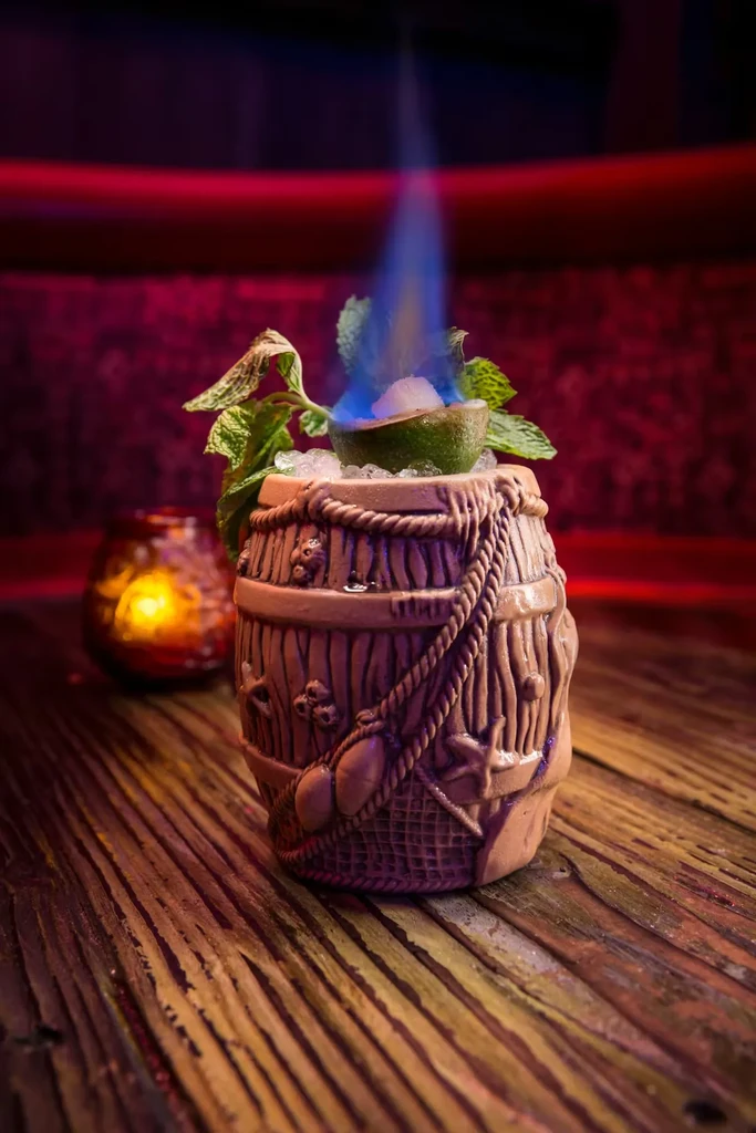 Elaborate barrel cocktail with blue flaming lime and mint.