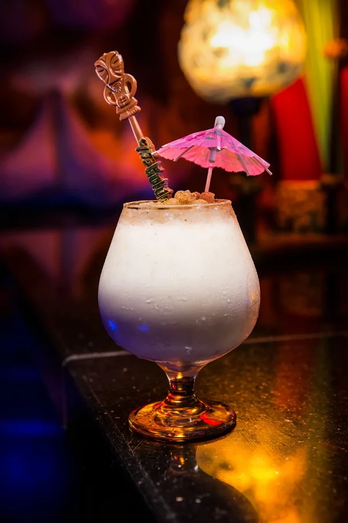 Frosty white cocktail in a goblet, garnished with an umbrella and tiki stirrer.