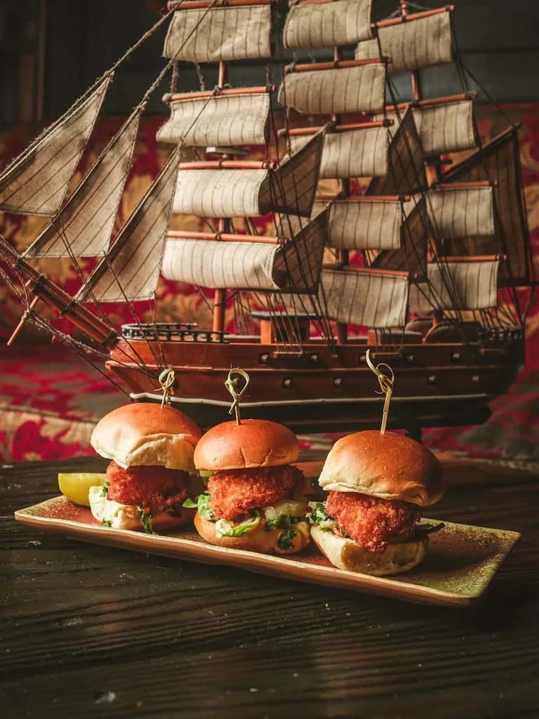Three breaded sliders, lime, and an antique sailing ship model.