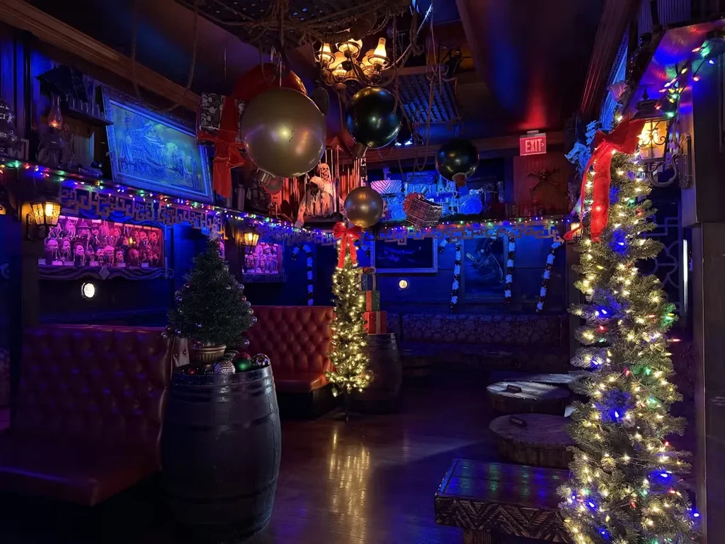 Eclectic bar interior with blue/purple lights, Christmas trees, and festive decorations.