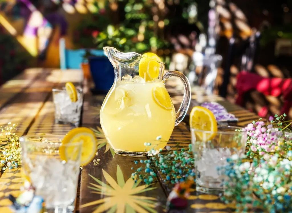 Pitcher of lemonade, three glasses, and colorful flowers on a rustic table.
