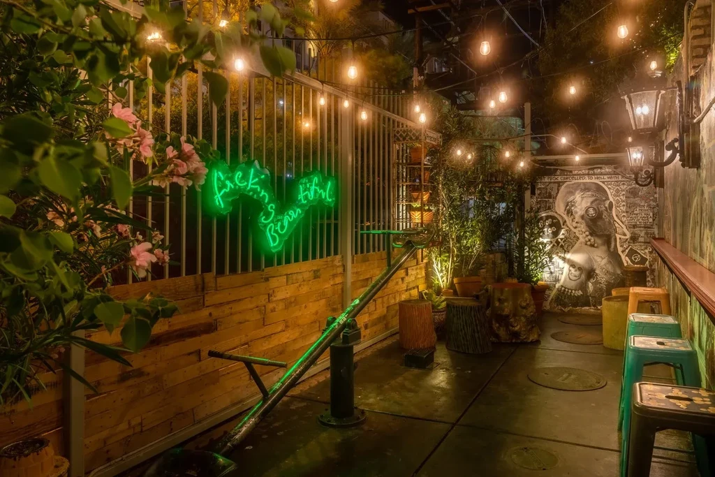 Night patio with "fucking beautiful" neon sign and gas mask mural.