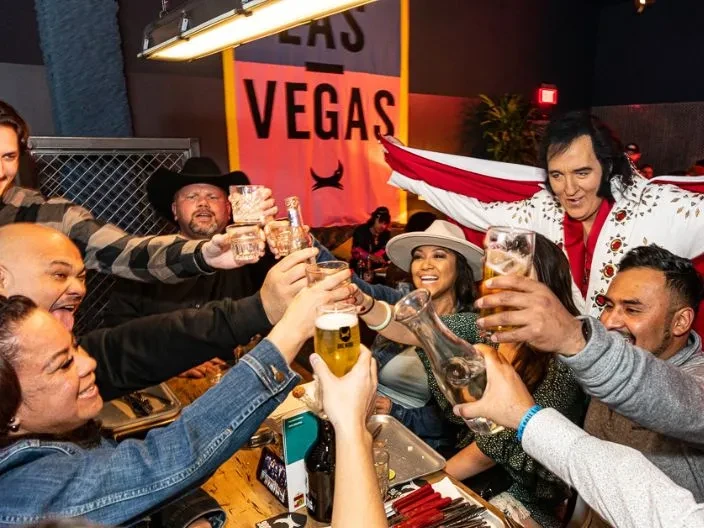 Smiling group toasting drinks with Elvis impersonator in Las Vegas.
