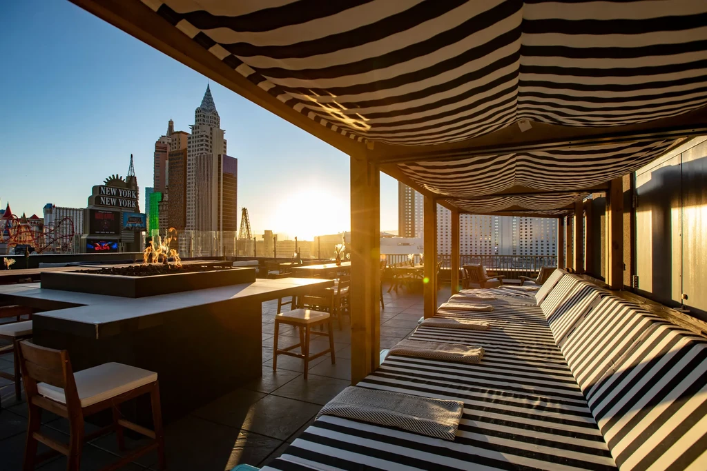 Sunset rooftop bar, fire pit, striped lounge chairs, Las Vegas skyline.
