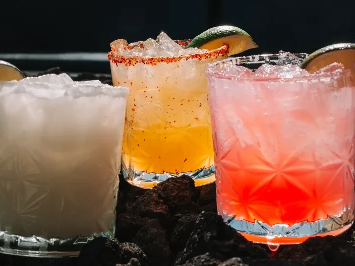 Three vibrant, icy cocktails with distinct rims and lime on dark stone.