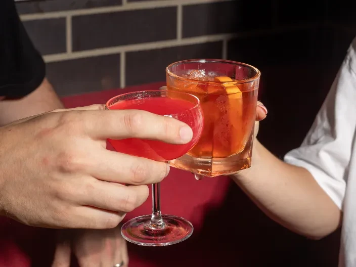 Two hands clinking different red and amber cocktails.