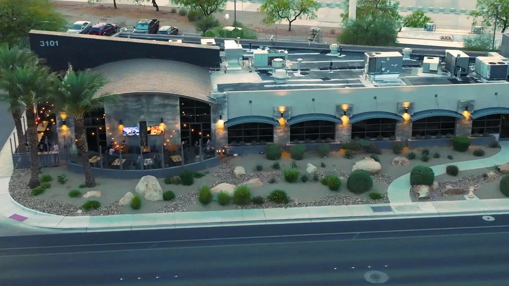 Aerial view of modern restaurant with lit patio and desert landscaping.