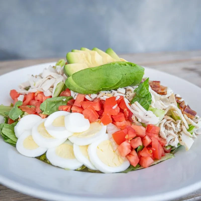 Large Cobb salad on a white plate with chicken, eggs, bacon, avocado.
