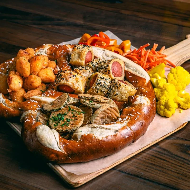 Appetizer platter of mini sausages, fried cheese, and vegetables on a pretzel.