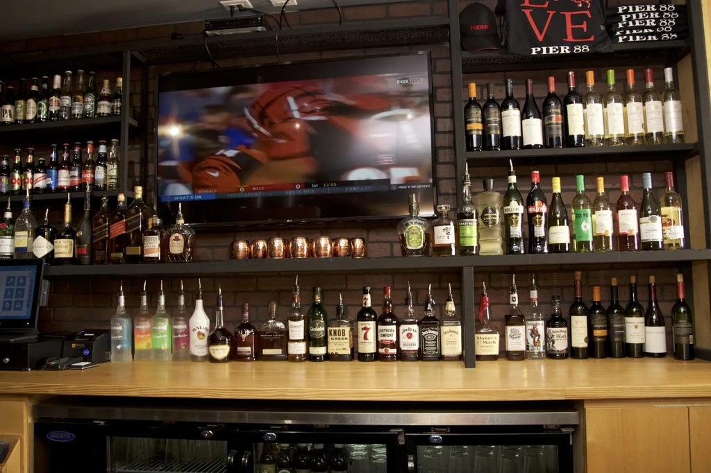 Restaurant bar with liquor bottles, sports on TV, and Pier 88 merch.