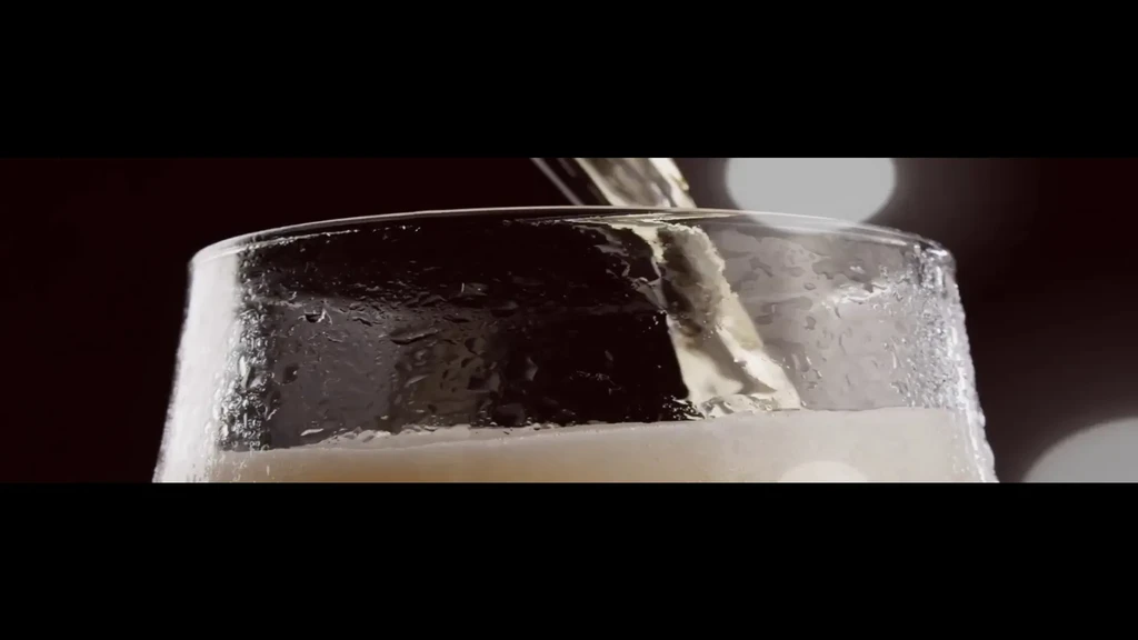 Frothy golden beer pours into a cold, condensing glass.