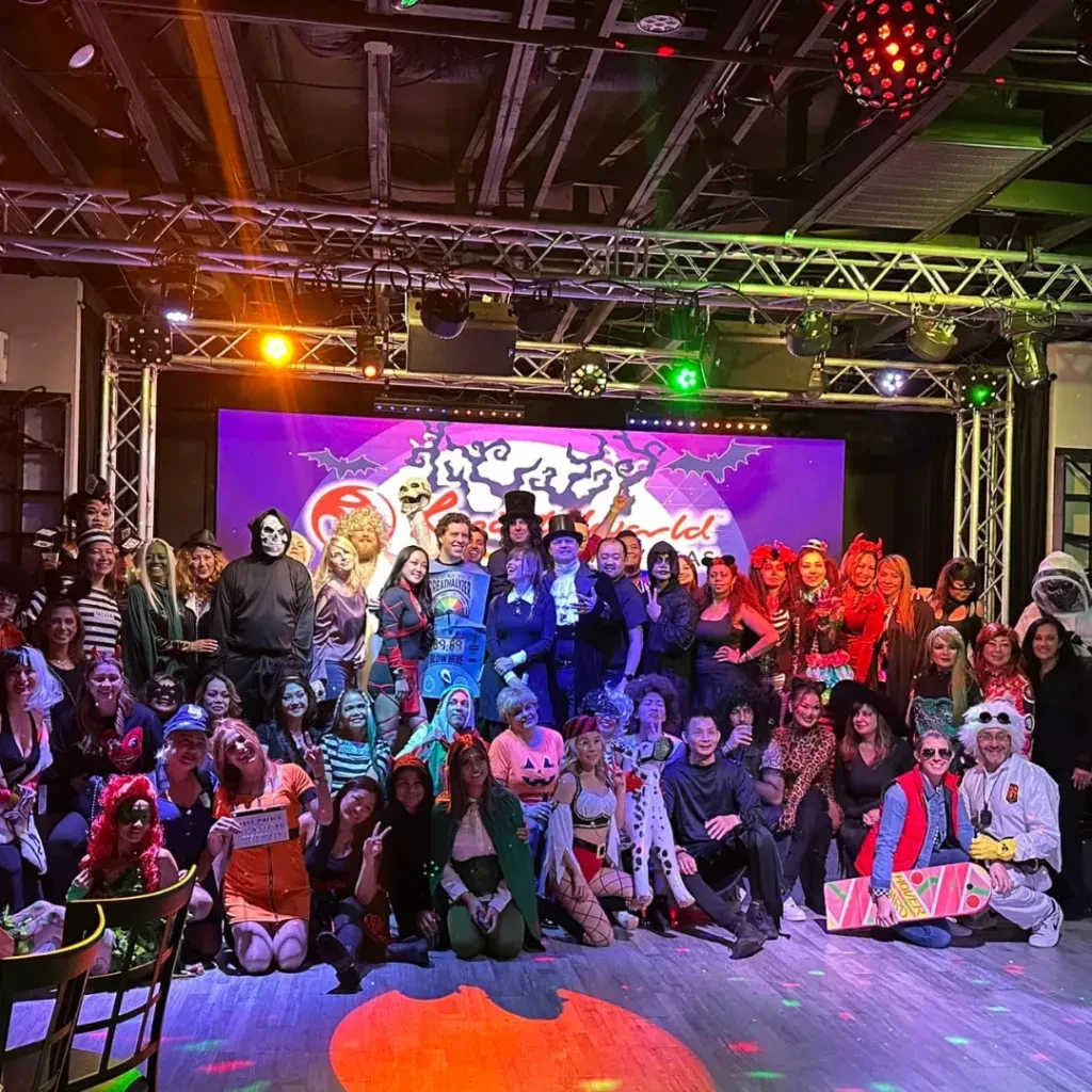 Large group of costumed people at a vibrant Halloween party with spooky decor.