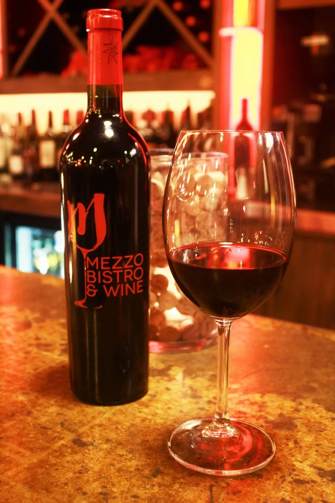 Mezzo Bistro red wine bottle, glass, and blurred bar background.