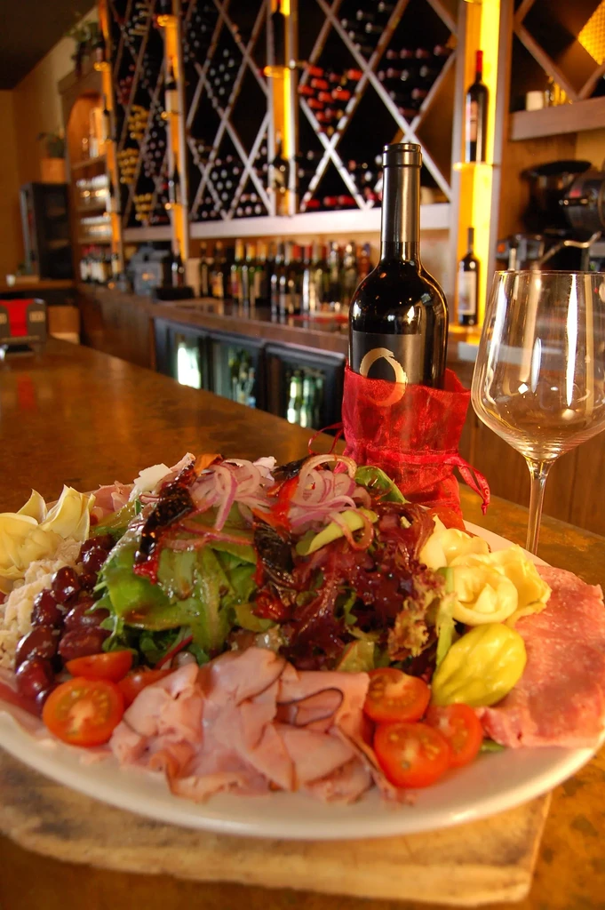 Close-up of an antipasto plate with wine on a bar counter.