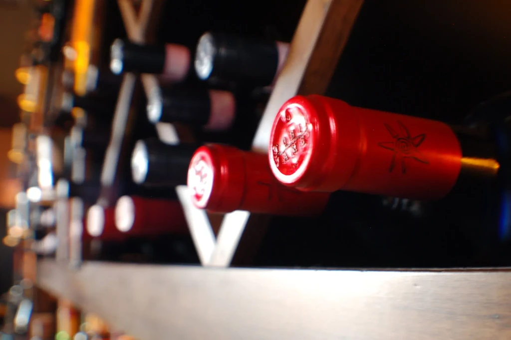 Close-up of wine bottles with red foil caps in a wooden rack.