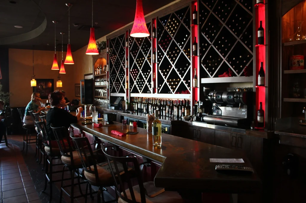 Upscale bar interior with a long counter and red-backlit wine display.