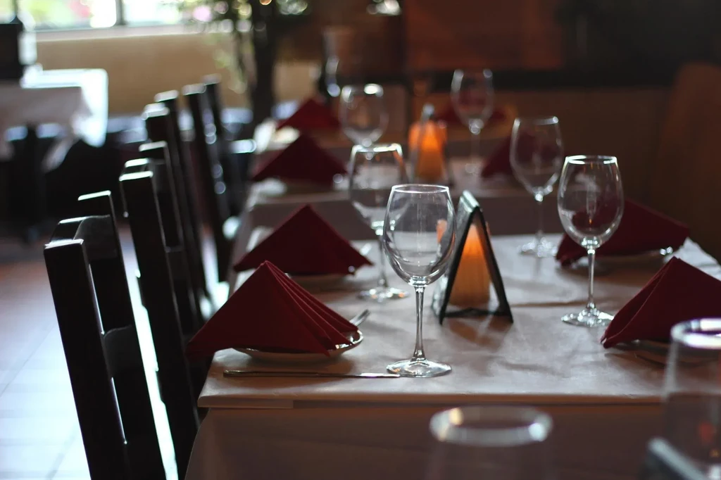 Set restaurant table with white tablecloth, glasses, and dark napkins.