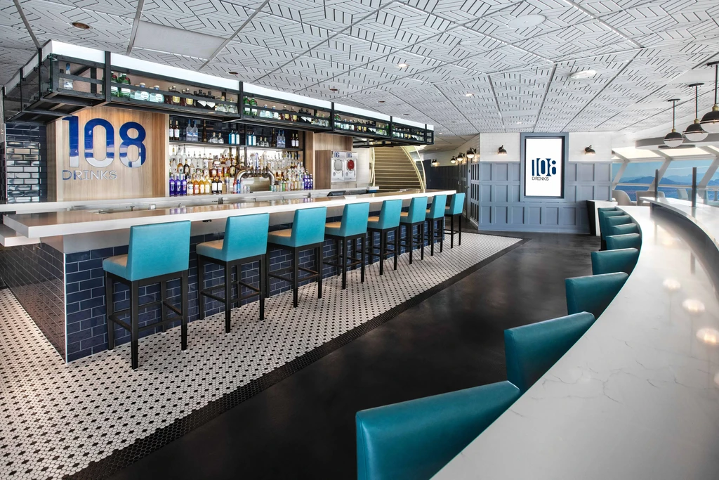 Modern bar with "108 DRINKS" sign, marble counter, and mountain view.