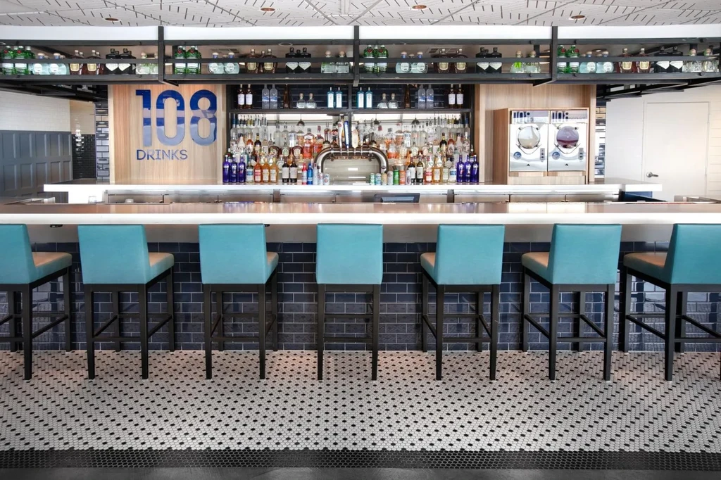 Modern bar with teal stools, extensive backbar, and "108 DRINKS" sign.