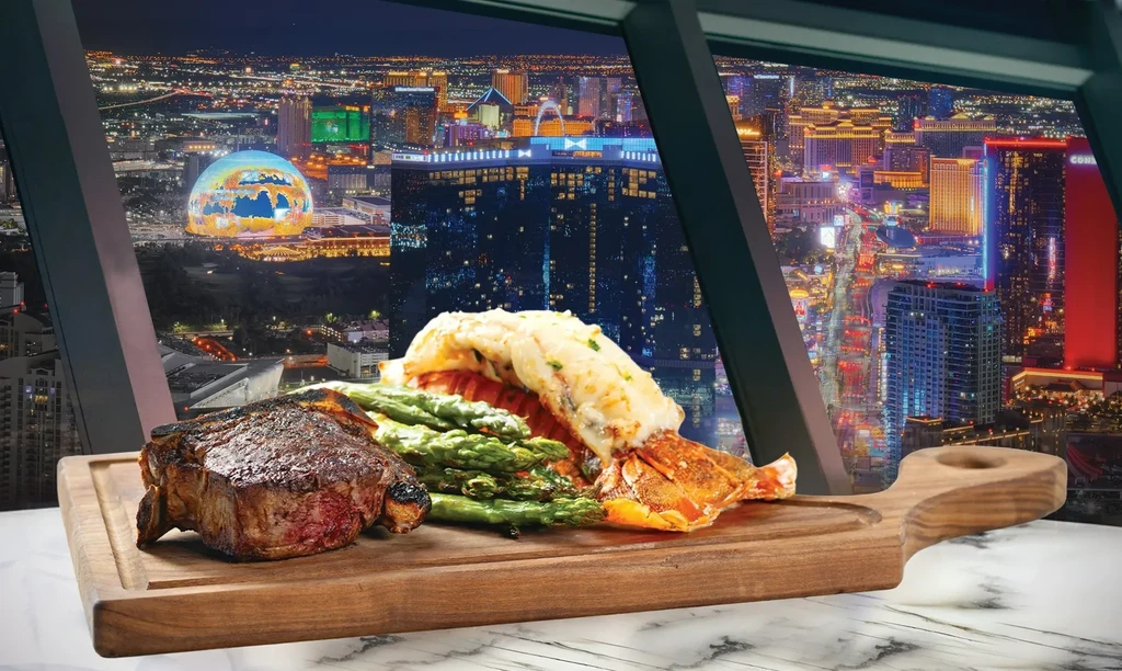 Steak, lobster, asparagus on wooden board overlooking a city at night.