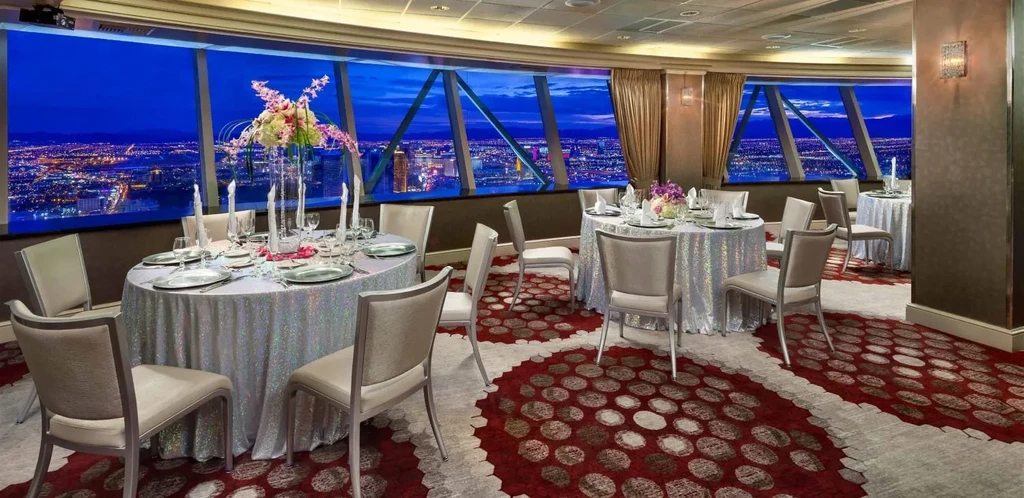 Empty high-rise restaurant, set tables, vast illuminated city skyline.