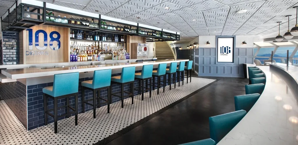 Modern bar and lounge with '108 DRINKS' sign, teal seating, scenic view.