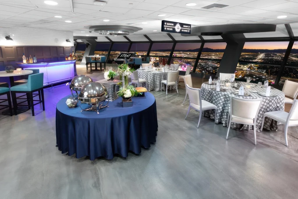Empty high-rise restaurant with buffet, modern bar, and illuminated city view.