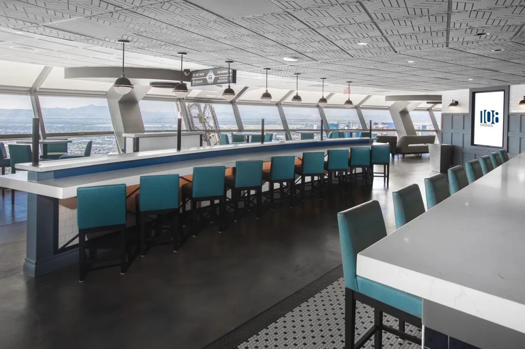Modern bar interior with curved bar, teal stools, and city views.