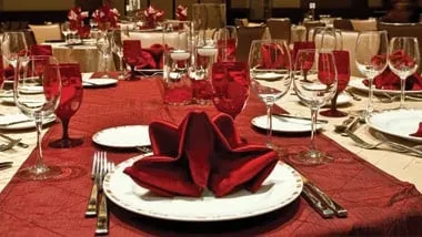Formal dining tables set with red linens, wine glasses, and silverware.