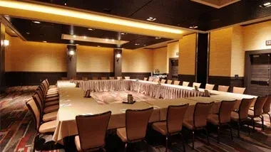 Empty meeting room with U-shaped table, white tablecloths, warm lighting.