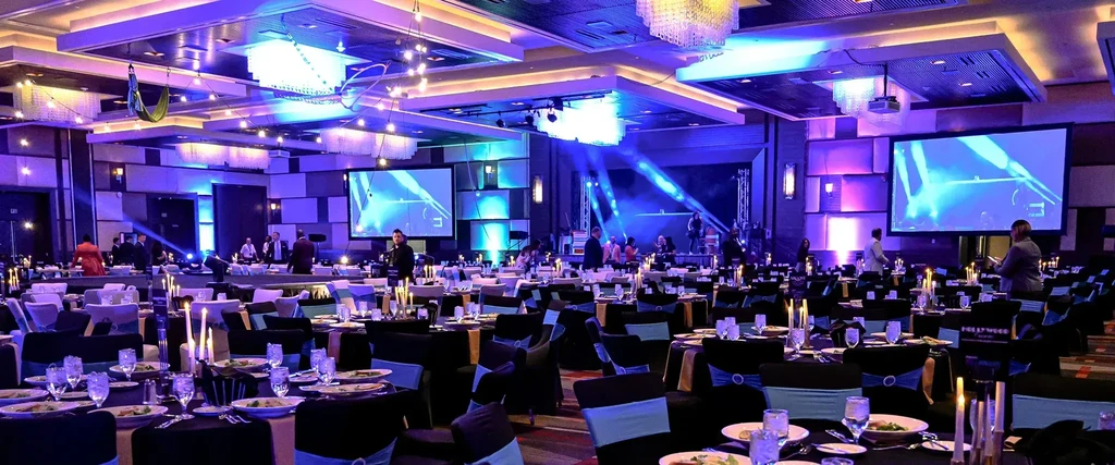 Event hall with black tables, blue-purple lighting, and a stage.