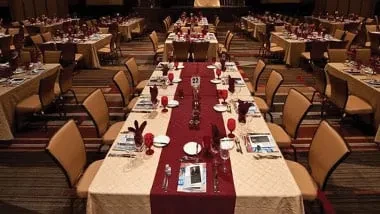 Long tables in formal banquet hall, set with gold and red.