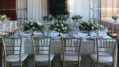 Formal dining table with white roses, green foliage, gold chairs.