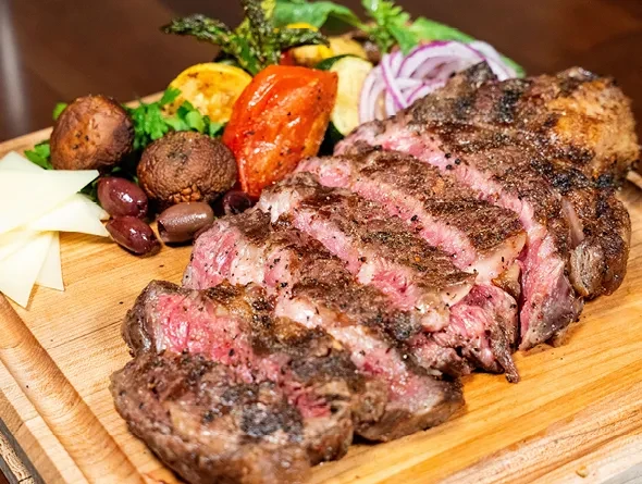 Sliced medium-rare steak with roasted vegetables, cheese, and olives.