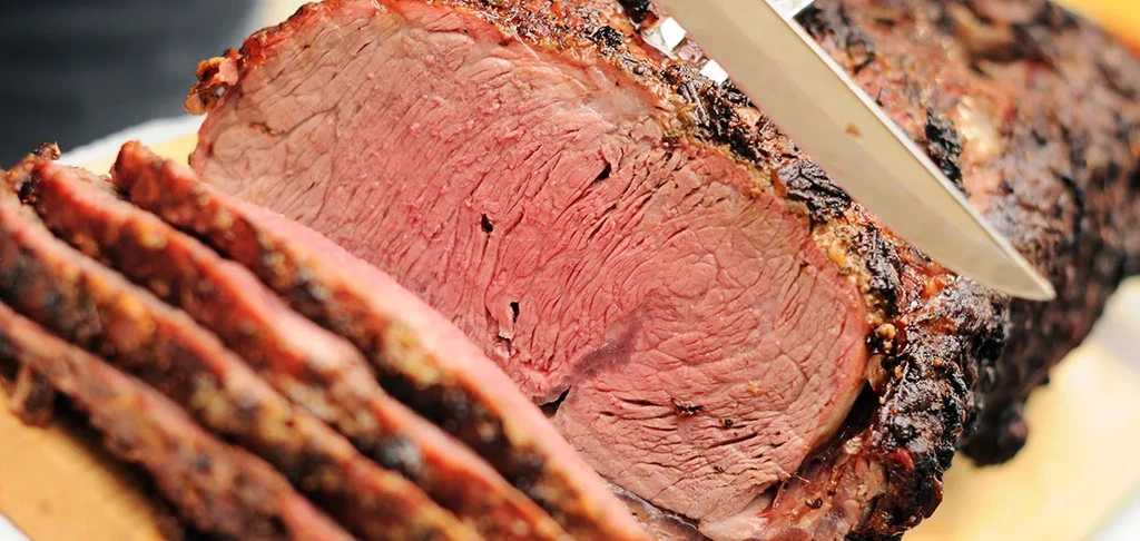 A knife slices roasted beef, revealing a medium-rare pink center.